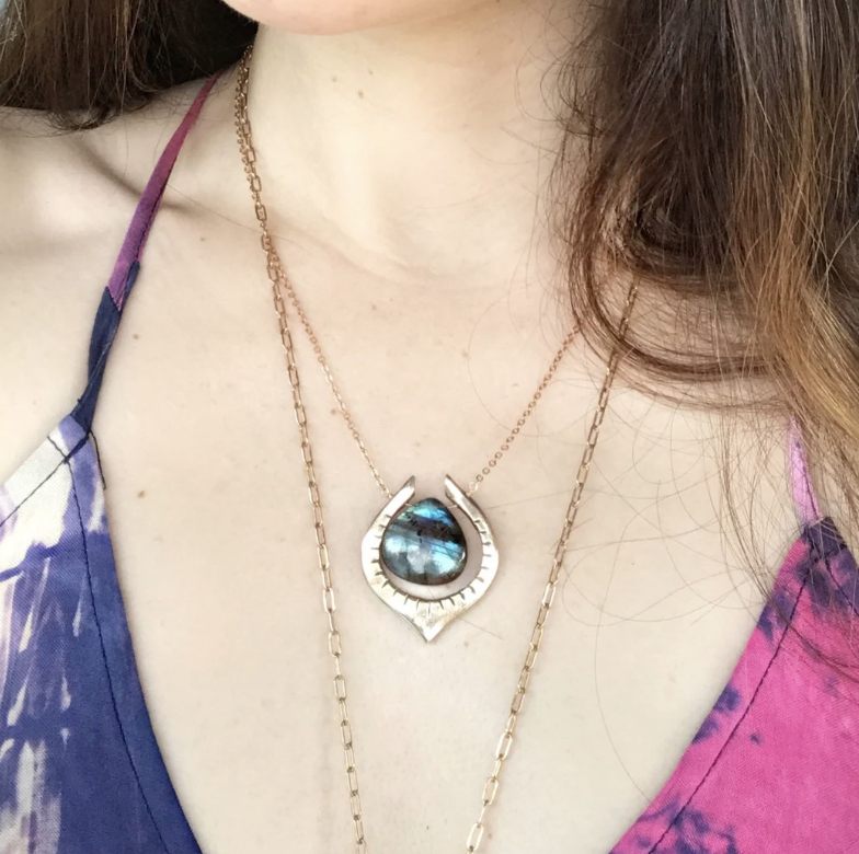Labradorite teardrop pendant with bronze frame on a gold chain, worn on chest with tie-dye top.